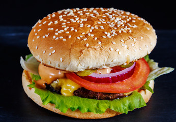 Hamburger with beef, cheese, onion, fresh salad and soft buns with sesame seeds on a dark background of natural stone.