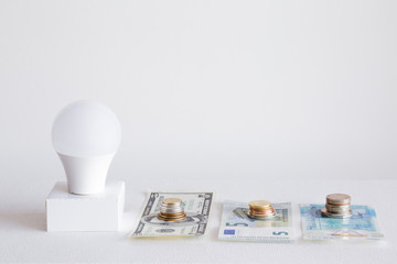 Led light bulbs with american dollar, english pound and euro money on the gray background. Concept of electricity payment in different countries. Empty place for a text and other ideas.