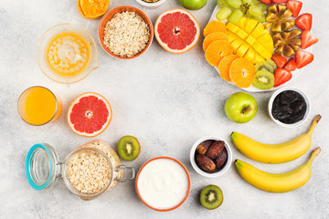 Healthy breakfast with oats, fruits, strawberries, mango, grapes, figs, yogurt and nuts arranged in a circle frame served on the grey white table, top view, copy space for text, selective focus
