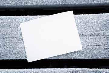 Icy white blank greeting card on the frozen wooden board. Mock up for holiday post cards for good mood and seasonal offers as advertising. Empty place for a text. Early morning.