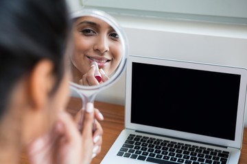Woman applying lipstick by laptop at home