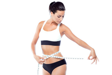 Beautiful young woman measuring her slim body over white background.