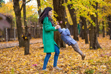 Mother with little son plays and smiles in park on background of colorful autumn fallen leaves