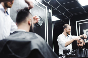 Fototapeta na wymiar Young handsome barber making haircut of attractive man in barbershop