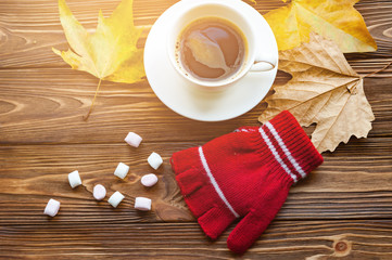 The red winter gloves with autumn leaves,marshmallows and cup of coffee on the wooden background.Fake color. Concept coziness and warmth.Instagram toned.