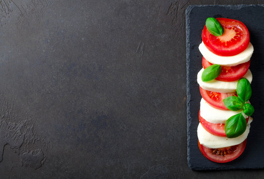 Fototapeta Sliced tomatoes and mozzarella on a slate plate, dark stone background. Top view, copyspace