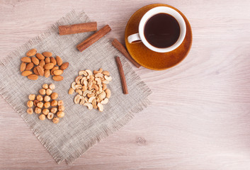  A cup of coffee, cinnamon, almonds, hazelnuts, cashew on a linen napkin.