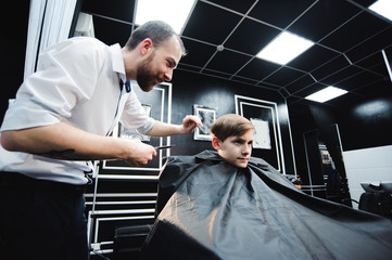 Fototapeta na wymiar Cute little boy is getting haircut by hairdresser at the barbershop