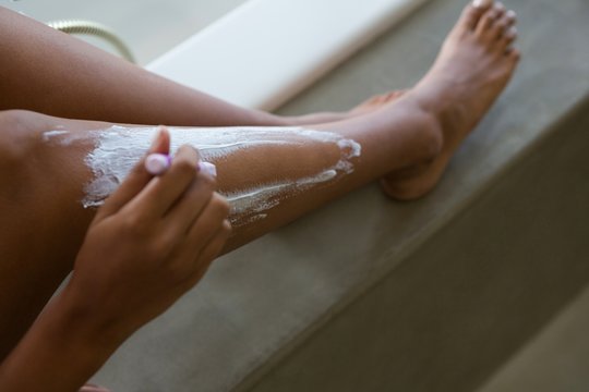 Low section of young woman shaving leg