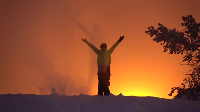 SLOW MOTION Unrecognizable person throwing snow up in the sky, raising arms proudly at golden sunset. Hiker outstretching arms victoriously against the orange sky at sunrise. Active people in winter