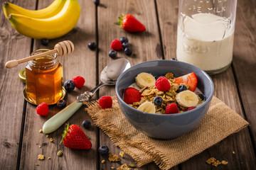 breakfast cereal shoot on wood boards angled view with raspberries blueberries bananas strawberries honey and a milk bottle and spoon landscape