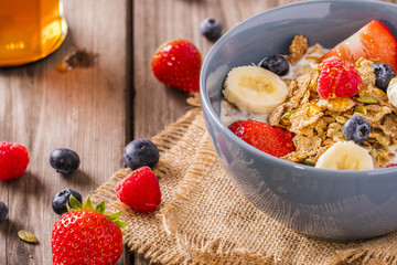 breakfast cereal shot close-up on linen cloth wood boards angled view with raspberries blueberries sliced bananas strawberries with hand swirling honey landscape