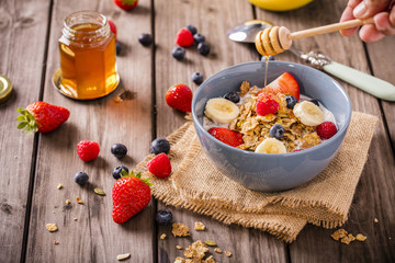 breakfast cereal shot on linen cloth wood boards angled view with raspberries blueberries sliced bananas strawberries with hand swirling honey landscape