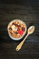Glass of granola with raspberries and yogurt on a black wooden table. Top view. Traditional American Breakfast