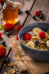breakfast cereal close-up shot on wood boards angled view with raspberries blueberries bananas strawberries and a milk bottle and spoon portrait
