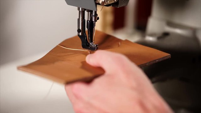 close up shot of the man's hands, who makes the leather product, the person puts the pattern on the sewing machine and begins to spend the product