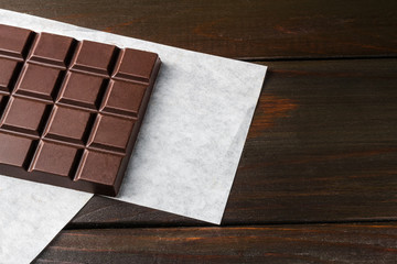 Bitter, dark chocolate bar on wooden planks background