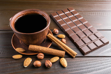 Hot black coffee in brown clay cup, dark chocolate bar, almond, hazelnut and cinnamon stick on...