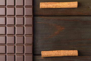 Bitter, dark chocolate bar and cinnamon stick on wooden background with space for text, top view