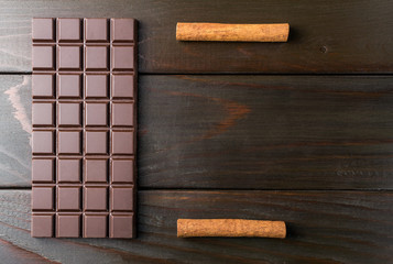 Bitter, dark chocolate bar and cinnamon stick on wooden background with space for text, top view