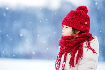 Adorable little girl having fun in beautiful winter park. Cute child playing in a snow. © MNStudio