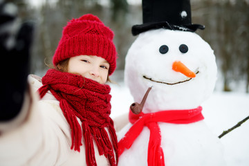 Adorable little girl building a snowman in beautiful winter park. Cute child playing in a snow.