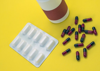 Pills spilling from an open bottle isolated on yellow background