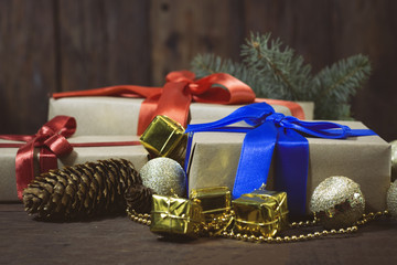 Gift boxes, a golden garland with balls, gifts and beads, a spruce branch, bumps. Focus on a gift with a blue ribbon