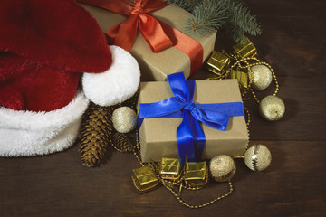 Santa Claus hat, boxes with gifts packed, spruce twig, golden beads, decorative boxes and balls, two bumps. Focus on the box with blue ribbon