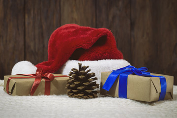 Santa Claus hat, gift boxes packed with craft paper tied with a red and blue ribbon, spruce branch, golden beads, decorative boxes and a ball, a cone. Focus on a box with a red ribbon