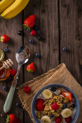 breakfast cereal shot on wood boards top view with raspberries blueberries bananas strawberries honey and a  spoon portrait