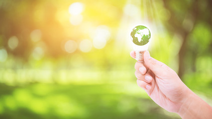 Hand holding a light bulb with energy green world inside on nature background, environment and...
