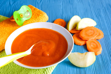 puree of baby carrot Apple on a wooden table spoon saucer white green pacifier napkin orange