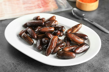 Ceramic plate with ripe dates on grey background