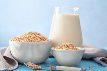 Bowls with oatmeal flakes and pitcher of milk on light background