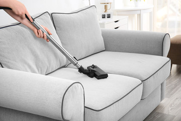Woman cleaning couch with vacuum cleaner at home