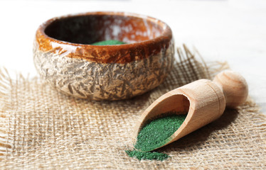 Scoop and bowl with spirulina powder on table
