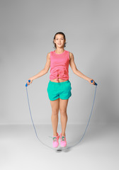 Young woman skipping rope on light background