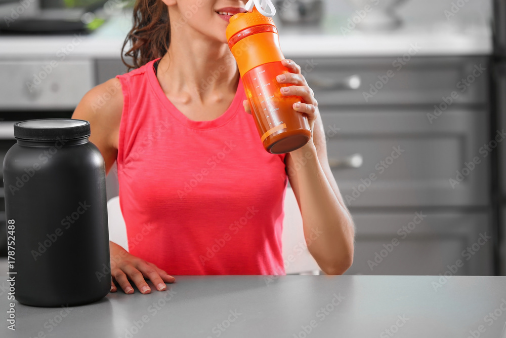 Poster Young woman drinking protein shake in kitchen