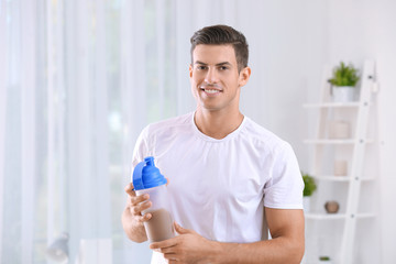 Young man holding bottle with protein shake indoors
