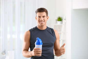 Young man holding bottle with protein shake indoors