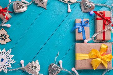 Christmas ornaments nestled in wooden plates blue. Garland around festive background. Top view of the bright gifts with bows on turquoise boards.