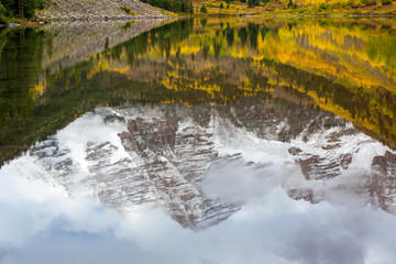 Reflection of Maroon Peak on Maroon Lake and aspen trees with its gold yellow leaves in fall foliage autumn season in a bright day light sunny day cloudy blue sky, Aspen, Colorado, USA.