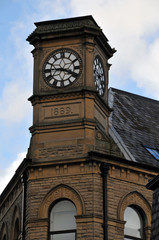 old clock on a stone tower with coulds and blue sky in hebden bridge west yorkshire
