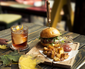 burger with potato on wooden plate with cocktail on wooden table