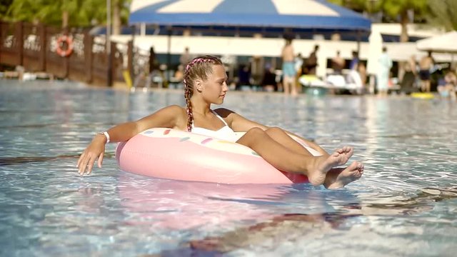 A young girl spends time in the pool, she sunbathes on an inflatable circle and swims in the water