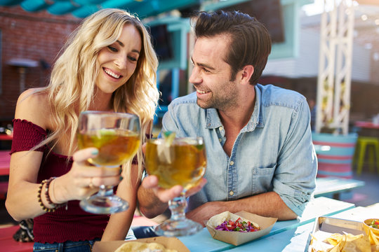 romantic couple making cheers with beer at outdoor mexican restaurant eating tacos