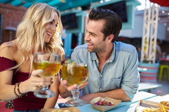 romantic couple making cheers with beer at outdoor mexican restaurant eating tacos