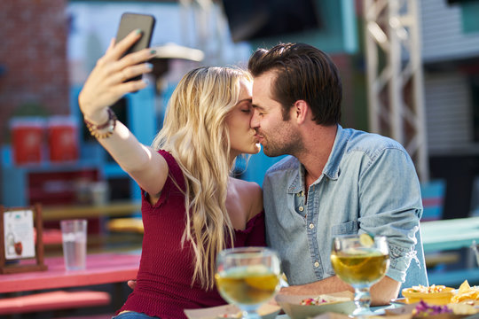 romantic couple taking selfie of themselves kissing while at mexican taco restaurant