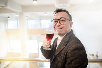 Happy Asian rich man smiling while holding a glass of red wine in the party hall